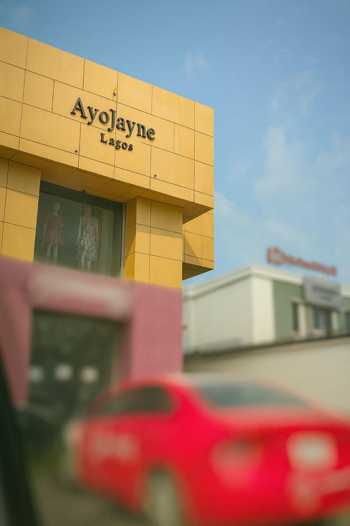 Gold building with 'Ayolayne Lagos' sign, blurred red car in foreground